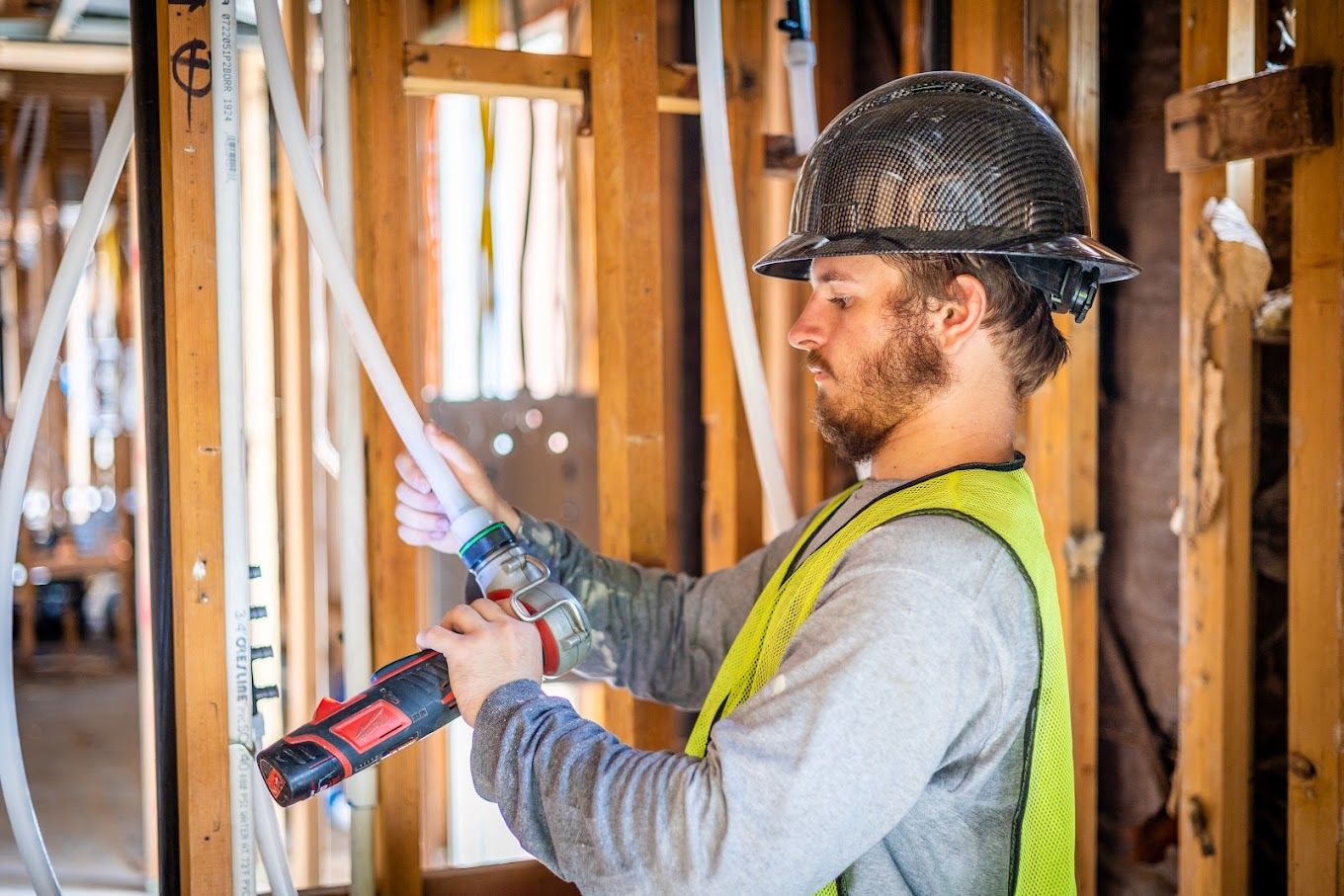 Plumber using a power tool to install PEX piping during a repiping project in a home under construction.