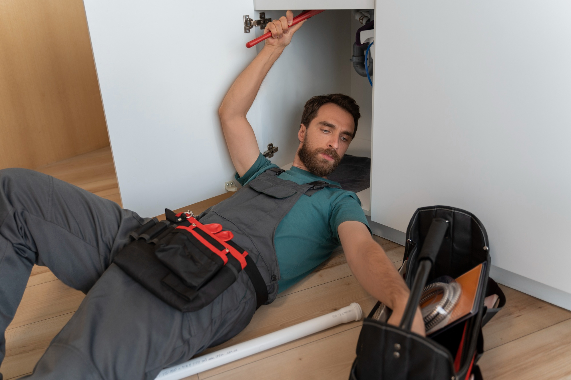 Plumber installing piping under sink with PEX tools and fittings