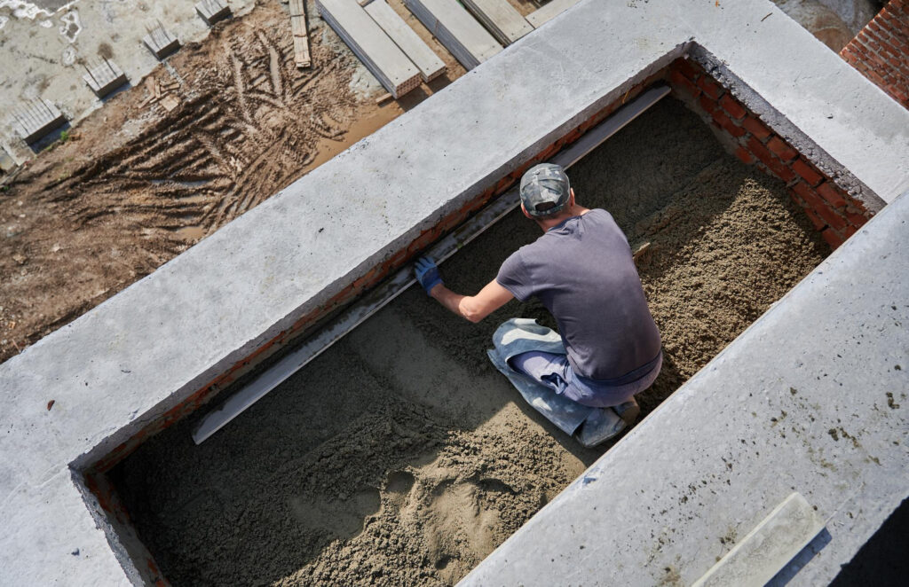 Slab being poured over plumbing by a worker outside placing foundation.