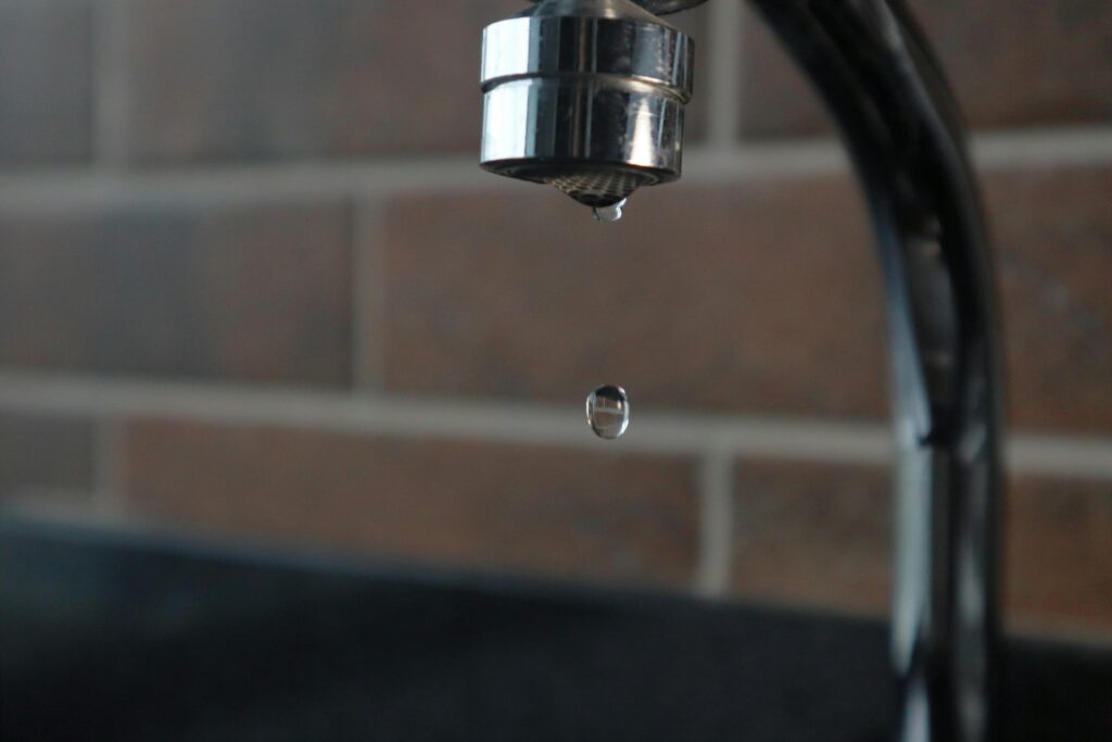 Close-up of a dripping kitchen faucet with a single water drop falling, indicating a plumbing leak that may require repiping.