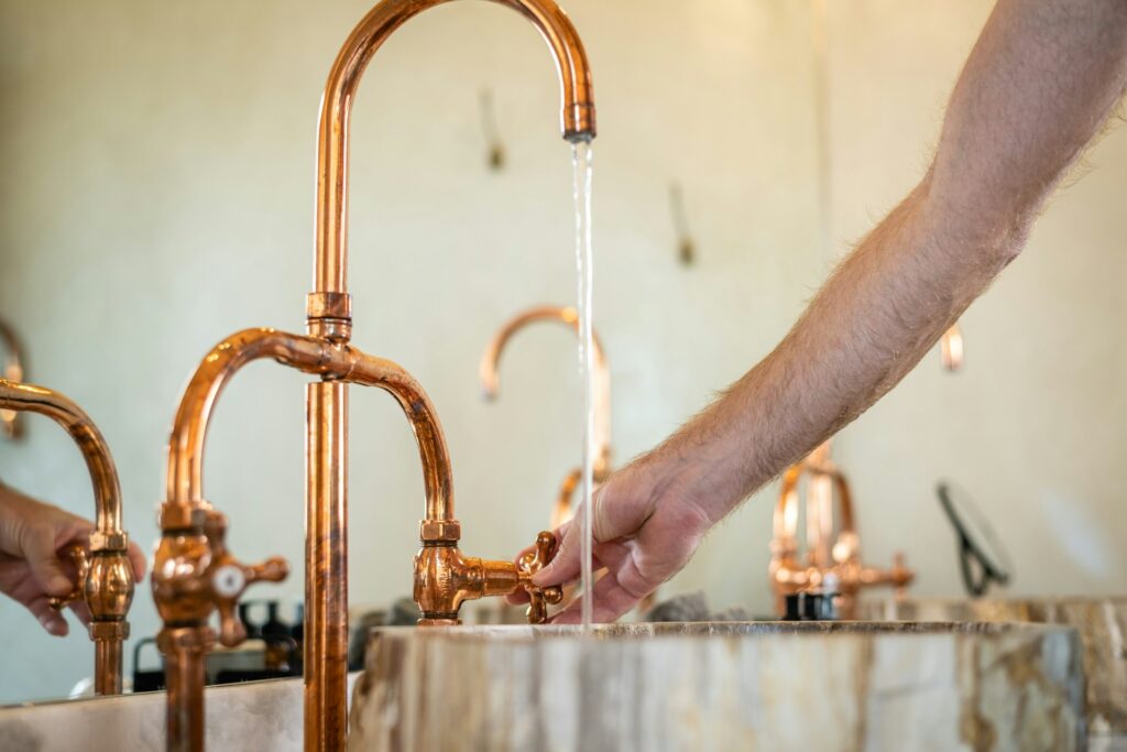 Plumber turning on a copper faucet over a stone sink, with water flowing to test new copper pipe installation.